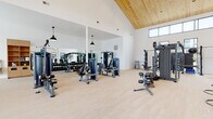 Located in Meridian, Idaho, this single-story fitness center is thoughtfully designed to support a wide range of workout styles and fitness goals. The space is defined by its striking vaulted ceiling finished in warm natural wood, which rises dramatically overhead and lends the interior an open, airy character. Crisp white walls and light hardwood-style flooring reinforce the clean, modern aesthetic throughout.

The strength training area is well-appointed with a full rack of dumbbells lining a floor-to-ceiling mirror wall, multiple selectorized resistance machines, benches, and a multi-functional cable station. A dedicated functional training zone features an overhead rig system with a heavy punching bag, TRX suspension trainers, and a colorful plate storage station, providing ample space for dynamic and combat-style training.

The cardio section lines a full wall of large steel-framed windows that frame views of the surrounding neighborhood, flooding the area with natural light. Treadmills, stationary bikes, stair climbers, and a rowing machine are all represented. Near the entrance, a built-in wood shelving unit and a water bottle filling station offer convenient amenities. The result is a bright, comprehensive, and professionally outfitted fitness facility.