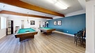 Located at 800 S Brea Blvd in Brea, California, this single-floor space offers a thoughtfully arranged layout encompassing a living room, a combined dining room and kitchen, a game room, and two bathrooms. The living room features plush carpeting, neutral walls, and natural light from windows with vertical blinds, creating a bright and welcoming atmosphere. The kitchen is well-equipped with white cabinetry, light quartz-style countertops, wood-look flooring, and black stainless appliances including an electric range, dishwasher, and refrigerator, alongside a double-basin sink beneath a window. The adjacent dining area accommodates a full-sized table, benefits from natural light through a large window overlooking greenery, and includes a ceiling fan overhead. A standout feature is the spacious game room, distinguished by exposed wood beam accents, a bold blue accent wall, wood-look flooring, and two full-sized pool tables with pendant lighting — ideal for recreation and entertaining. Both bathrooms are finished with white vanities, light countertops, wood-look flooring, and large mirrors, maintaining a clean and consistent aesthetic throughout. Textured ceilings are present across the space, adding a classic touch to this functional and versatile Brea property.