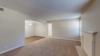 This single-story residence offers a well-organized layout with a variety of functional spaces throughout. The living area is generously proportioned, featuring neutral-toned carpet, soft gray walls, and a textured ceiling. A white-mantled fireplace serves as a focal point, flanked by windows dressed with horizontal blinds that allow ample natural light. The space flows openly into an adjoining area with hardwood-style flooring, illuminated by a pendant light fixture.

The galley-style kitchen is efficiently designed, featuring white cabinetry with brushed nickel hardware, light granite-look countertops, a double sink, and black appliances including a range and refrigerator. Track lighting overhead and hardwood-style flooring complete the kitchen's clean, functional aesthetic.

The bedrooms are carpeted and finished with neutral tones, each equipped with ceiling fan and light combinations. One bedroom features a window with outdoor views and direct access to a spacious walk-in closet outfitted with wire shelving on both sides. A second bedroom includes a louvered double-door closet. The bathroom is equipped with a full-size soaking tub and shower combination with chrome fixtures. Throughout, textured ceilings and white baseboards provide a consistent, cohesive finish.