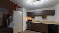 Located at 818 Strickland Pl in Wilmington, NC, this two-story home offers a practical and well-organized layout across two distinct levels. The kitchen is equipped with dark wood-toned cabinetry providing ample upper and lower storage, a stainless steel gas range, a built-in sink with standard faucet, and a dishwasher. A track lighting system illuminates the space, and wood-look hard flooring runs throughout the main level, adding a warm, cohesive feel. An adjacent area on the lower floor features additional living space with the same durable flooring and a window unit for climate control. Natural light filters in through a set of wide windows, offering views of the surrounding neighborhood greenery. The bathroom includes wood-look flooring, slate-toned upper cabinetry, and brushed nickel hardware and towel bars for a clean, functional finish. Upstairs, the upper level features plush carpeting underfoot and a vaulted, angled ceiling that adds architectural character and a sense of openness. An open railing overlooks the staircase, connecting the two floors with an airy feel. A ceiling fan with a light fixture serves the upper level. The textured ceilings throughout contribute a classic residential character to the overall space.