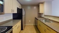 Located at 160 Pleasant St in Malden, Massachusetts, this single-floor residential unit offers a practical and well-organized layout designed for comfortable everyday living. The open living area is finished with neutral-toned carpet and features a large window that allows natural light to fill the space while offering views of the surrounding building exterior. A structural beam detail adds a subtle architectural element to the room's profile.

The kitchen is efficiently designed in a galley-style configuration, outfitted with light wood cabinetry, dark granite-style countertops, stainless steel appliances including a refrigerator, gas range, and dishwasher, and a double stainless steel sink. The kitchen is accessible from the living area via a half-wall pass-through, creating an open and connected feel. Flooring in the kitchen transitions to a durable vinyl-style surface.

The bedroom is a quiet, carpeted space with neutral walls and architectural beam detailing, providing a calm and functional retreat. The full bathroom features a combination tub and shower, a wood-toned vanity with granite-style countertop, a large wall mirror, and clean white finishes throughout. The unit also includes a full entry door with hardware and additional closet or utility storage, as seen in the floor plan overview.