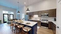 Located at 615 E Corcoran Ave in Milwaukee, Wisconsin, this well-appointed 2-bedroom, 2-bathroom residence offers a thoughtfully designed single-level layout with an open-concept kitchen and living area. The kitchen is a standout feature, showcasing rich dark-stained cabinetry, a textured tile backsplash, stainless steel appliances, light quartz countertops, and a bold navy island with seating for four — all illuminated by striking pendant lighting beneath soaring ceilings. The living area opens via French doors to the outdoors and benefits from transom windows that draw in abundant natural light. Both bedrooms are generously proportioned, with the spacious primary bedroom featuring tall ceilings, plush carpet flooring, and a large window with outdoor views. The two bathrooms are elegantly finished — one includes a dual-sink vanity with dark wood cabinetry and backlit mirrors, while the second offers a full tub-shower and light gray cabinetry with wood-tone flooring. Three closets provide ample storage throughout. A dedicated laundry room includes a stacked washer and dryer with a utility sink. Light hardwood-style flooring flows through the main living spaces, tying together the modern, clean aesthetic of the home.