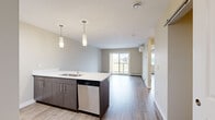 Located at 5000 Green Jewel Blvd in Regina, Saskatchewan, this well-appointed 2-bedroom, 1-bathroom unit offers a thoughtfully designed open-concept layout across a single floor. The combined kitchen and living area serves as the heart of the unit, where a sleek peninsula with a white quartz countertop and an undermount sink anchors the space. The kitchen is outfitted with stainless steel appliances — including a refrigerator, electric range, over-the-range microwave, and dishwasher — complemented by white upper cabinetry, dark lower cabinetry, and stylish pendant lighting. Wood-look luxury vinyl plank flooring flows throughout the entire unit, adding warmth and continuity. The living room opens directly to a private balcony through sliding glass doors, offering views of the surrounding neighborhood. A wall-mounted mini-split unit provides efficient climate control. Both bedrooms feature neutral toned walls, wood-look flooring, and baseboard heating, with one bedroom offering a large window overlooking the outdoors and the other featuring a built-in closet with a sliding door and wire shelving. The full bathroom includes a soaker tub with a tub surround. This unit presents a clean, modern aesthetic throughout.