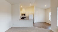 This single-floor residence offers a bright, open layout designed for comfortable everyday living. The main living area is generously sized, featuring soft wall-to-wall carpeting, vaulted ceilings that enhance the sense of openness, and multiple windows with blinds that allow abundant natural light to fill the space. A wall-unit HVAC system provides climate control directly in the living area.

The kitchen is positioned in an efficient peninsula layout, partially open to the living space. It features white cabinetry extending to the upper walls, gray laminate countertops, a stainless steel microwave, an electric range, a full-size white refrigerator, a dishwasher, and a built-in sink. Wood-look flooring runs throughout the kitchen area, providing a clean contrast to the carpeted living spaces.

Two carpeted bedrooms offer comfortable retreats, each with natural light from windows dressed with blinds. One bedroom includes a closet with a sliding door and built-in shelving and rod for organization. The second bedroom features a spacious closet with a paneled sliding door.

The residence includes two full bathrooms, both finished with warm earth-toned tile flooring and white vanity cabinetry with gray countertops. One bathroom features a shower/tub combination, while the other provides a vanity and toilet in a clean, functional layout.
