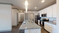 Haven on Tucker is a thoughtfully designed single-floor residence that blends modern finishes with a comfortable, functional layout. The open-concept kitchen serves as the heart of the home, showcasing a large granite-topped island with a built-in sink and bar seating, white shaker cabinetry, a light blue subway tile backsplash, and a full suite of stainless steel appliances including a refrigerator, range, and microwave. Elegant pendant lighting illuminates the island, complementing the recessed ceiling lights throughout. Rich, dark hardwood-style flooring flows seamlessly through the kitchen and living areas, creating a cohesive aesthetic. The living room is bright and inviting, benefiting from natural light through windows and a glass-paned door that opens to the outside. Crown molding details along the ceiling add a refined architectural touch. The bedrooms offer plush carpeting and clean, neutral walls, with the primary bedroom featuring a bright window with views to the exterior. The bathroom is well-appointed with granite countertops, white cabinetry, and light wood-tone flooring. A dedicated laundry area is also included within the unit. Overall, the space presents a clean, contemporary atmosphere with quality finishes throughout.