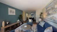 This single-floor residence offers a thoughtfully designed layout that balances comfort and functionality throughout. The open-concept living area serves as the heart of the home, featuring rich wood-look flooring, a distinctive teal accent wall, and a ceiling fan overhead. A sliding glass door floods the space with natural light and opens to an outdoor view, while built-in shelving adds both character and storage. The living area flows seamlessly into the dining space, which is anchored by a ceiling fan and connects directly to the galley-style kitchen. The kitchen is well-equipped with white upper cabinetry, gray lower cabinets, generous countertop space, a double sink, and black appliances — all set on wood-look flooring. The bedroom is a calm retreat with plush carpeting, a bright window with blinds, and ample wall space. Adjacent to the bedroom is a bathroom featuring a shower-tub combo and wood-look flooring. A second full bathroom includes a dual-sink vanity with gray cabinetry and a spacious countertop. An additional carpeted room with a window offers flexibility as a home office, den, or guest space. Throughout, the neutral palette and cohesive design create a welcoming and functional environment.
