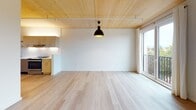 This single-floor space showcases a thoughtfully designed modern interior defined by a striking architectural feature: exposed natural wood plank ceilings that run throughout, adding warmth and texture to the clean, minimalist aesthetic. The open-concept living and dining area is bright and airy, benefiting from large windows and a sliding glass door that invites natural light and provides outdoor views. Light hardwood flooring extends across the main living spaces, complementing the warm ceiling tones.

The kitchen is well-appointed with flat-front wood cabinetry, white quartz countertops, a tiled backsplash, stainless steel appliances including a dishwasher and range, and open metal shelving for practical storage. A peninsula-style layout defines the kitchen's boundary with the living area.

The bedrooms feature soft grey carpeting, wall-mounted sconce lighting, and continued wood ceiling detailing, creating a cozy and intimate atmosphere. Windows in each room allow for natural light and ventilation.

The bathroom maintains the space's clean design language with light hardwood-style flooring, a floating wood vanity, a frosted window for privacy, and a shower with curtain enclosure. Grab bars and thoughtful fixtures reflect a functional, accessible layout throughout.