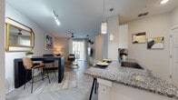This well-appointed single-floor residence offers a thoughtfully designed open-concept layout that seamlessly connects the kitchen, dining, and living areas. The kitchen serves as a focal point, showcasing granite countertops, white shaker-style cabinetry, a mosaic tile backsplash, stainless steel appliances, and a peninsula island with bar seating — illuminated by a modern pendant light fixture. Light wood-style flooring runs throughout the main living areas, contributing to a clean, cohesive aesthetic.

The living room is bright and welcoming, benefiting from a sliding glass door that opens to a private balcony, allowing natural light to flow freely into the space. A ceiling fan adds both function and style to the room.

The residence includes two bedrooms, each carpeted for comfort and equipped with large windows that frame views of the surrounding greenery. The bedrooms offer ample natural light and a calm, neutral color palette.

The bathroom features a full tub-shower combination with tile surround and chrome fixtures, maintaining a clean and practical design consistent with the rest of the home. Overall, the space presents a modern, move-in-ready residence with quality finishes and a bright, airy atmosphere throughout.