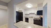 Located at 6901 River Run Dr in East Lake, Florida, this single-floor unit presents a clean, functional layout finished with light neutral tones and tile flooring throughout. The space features a textured ceiling and consistent gray-painted walls that create a cohesive, understated aesthetic from room to room.

The kitchen is a practical highlight, featuring white cabinetry, granite-style countertops, and a breakfast bar that opens to the adjacent living area. Black appliances, including a refrigerator, dishwasher, range, and microwave, provide a strong contrast against the white cabinetry. Overhead lighting illuminates the workspace efficiently.

The living area is generously proportioned, with large-format tile flooring and a sliding glass door that opens to a balcony overlooking mature trees, allowing natural light to fill the space. A secondary room with a window and matching tile flooring offers additional flexible living space.

The bathrooms are finished with granite-topped white vanities, large mirrors, and tile flooring, maintaining the consistent design language found throughout the unit. Hallways connect the rooms in a straightforward layout, as illustrated by the 3D floor plan, making the overall flow of the space easy to navigate.