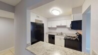 Located at 6901 River Run Dr in East Lake, Florida, this single-floor unit presents a clean, functional layout finished with light neutral tones and tile flooring throughout. The space features a textured ceiling and consistent gray-painted walls that create a cohesive, understated aesthetic from room to room.

The kitchen is a practical highlight, featuring white cabinetry, granite-style countertops, and a breakfast bar that opens to the adjacent living area. Black appliances, including a refrigerator, dishwasher, range, and microwave, provide a strong contrast against the white cabinetry. Overhead lighting illuminates the workspace efficiently.

The living area is generously proportioned, with large-format tile flooring and a sliding glass door that opens to a balcony overlooking mature trees, allowing natural light to fill the space. A secondary room with a window and matching tile flooring offers additional flexible living space.

The bathrooms are finished with granite-topped white vanities, large mirrors, and tile flooring, maintaining the consistent design language found throughout the unit. Hallways connect the rooms in a straightforward layout, as illustrated by the 3D floor plan, making the overall flow of the space easy to navigate.