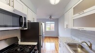 Located at Mid Island Apartments in Bay Shore, NY, this single-floor residence combines classic charm with modern updates throughout. Warm, polished hardwood flooring flows seamlessly across the living areas and bedrooms, creating a cohesive and inviting atmosphere. The walls are painted in soft, cool gray-blue tones that lend the space a calm, airy feel.

The galley-style kitchen is well-appointed with crisp white shaker cabinetry, marble-look countertops, a gray subway tile backsplash, and a full suite of stainless steel appliances, including a gas range, built-in microwave, and refrigerator. A ceiling fan overhead and a window offering views of the surrounding community complete the kitchen area.

The living areas are generously proportioned, featuring large windows that draw in abundant natural light and offer views of the neighborhood. Ceiling fans and baseboard heating ensure year-round comfort, and a wall-mounted air conditioning unit provides additional climate control.

Bedrooms are bright and well-sized, with hardwood floors continuing throughout and access to a dedicated closet with built-in shelving for ample storage. The bathroom features a white vanity with marble-look countertop, a mirrored medicine cabinet, and clean, updated finishes. The overall design is functional, modern, and move-in ready.