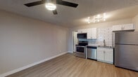 This single-floor unit offers a clean, modern aesthetic throughout its open layout. The main living area is spacious and versatile, featuring light-toned laminate wood flooring, neutral wall tones, and a ceiling fan with integrated lighting. A window with blinds allows natural light to fill the room, while a wall-mounted A/C unit provides climate control. The textured ceiling adds a classic touch consistent throughout the space.

The kitchen is thoughtfully designed and flows seamlessly from the living area. It is outfitted with a full suite of stainless steel appliances, including a refrigerator, electric range, over-the-range microwave, and dishwasher. White shaker-style cabinetry provides ample storage, while the white subway tile backsplash adds a stylish, contemporary accent. A stainless steel sink with a modern pull-down faucet and dark countertops complete the functional and attractive kitchen setup. Track lighting illuminates the workspace effectively.

The bathroom features a full-size tub and shower combination with a square rainfall-style showerhead, white surrounds, and brushed nickel fixtures. A toilet and towel bar round out the clean, no-frills design. Overall, the unit presents a refreshed, move-in-ready interior with consistent finishes and practical amenities throughout.