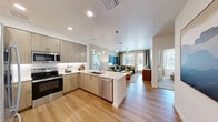 Located in Phoenix, AZ, this well-designed 2-bedroom, 2-bathroom residence offers a thoughtful single-floor layout with modern finishes throughout. The open-concept kitchen and living area serves as the heart of the home, featuring light wood-tone cabinetry, a white quartz peninsula with bar seating, stainless steel appliances including a French door refrigerator, electric range, microwave, and dishwasher, all complemented by stylish globe pendant lighting. Light hardwood-style flooring flows seamlessly through the main living areas, while large windows invite abundant natural light into the living room, which offers views of the surrounding community. The primary bedroom features soft carpet, a ceiling fan, large windows with exterior views, and a calming sage green accent wall. It is served by a spacious en suite bathroom with dual sinks, a long wood-tone vanity, white quartz countertop, and a glass-enclosed walk-in shower. The primary suite also includes a generous walk-in closet with built-in shelving and dual hanging rods. The second bedroom is equally well-appointed, and the second bathroom features a combined tub and shower with tile surround, a single vanity, and hardwood-style flooring. A convenient hallway connects all areas of this clean, contemporary home.