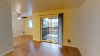 This single-floor unit offers a practical and comfortable layout within a well-utilized footprint. The living area is a standout feature, highlighted by warm hardwood-style flooring that runs throughout and soft yellow walls that create a bright, welcoming atmosphere. A sliding glass door serves as the focal point of the main living space, fitted with vertical blinds and providing direct access to a private outdoor deck. The deck overlooks lush, mature trees, offering a sense of privacy and a natural backdrop. An additional window positioned on the adjacent wall enhances natural light, further brightening the interior. The textured ceiling adds subtle visual character, while a ceiling fan ensures year-round comfort. Wall-mounted heating units are conveniently positioned within the living space, providing efficient climate control. The overall design is straightforward and functional, with clean lines and neutral finishes that offer flexibility for personalization. The unit's single-floor layout ensures easy accessibility and a cohesive flow between spaces. With its combination of indoor comfort and outdoor access, this 1-bedroom, 1-bathroom unit presents a well-rounded living environment.