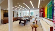 Located at 2020 Morton St in Charlotte, NC, this single-floor amenity lounge is a thoughtfully designed communal space that blends modern architecture with eclectic, art-forward interiors. The open layout is anchored by large-format porcelain tile flooring and a ceiling lined with sleek recessed linear lighting that illuminates the expansive floor plate evenly throughout.

The main lounge area features a substantial leather sectional sofa paired with white cube coffee tables and colorful accent chairs arranged atop a vibrant area rug. A dedicated media wall clad in warm wood slat paneling houses a large flat-screen TV, providing a comfortable entertainment hub. Adjacent to the lounge, a full-length bar counter with herringbone detailing and woven pendant lights overhead seats several guests on mid-century style barstools, with windows framing natural views beyond.

A billiards table occupies a central position in the space, while a foosball table near a glass sliding door offers additional recreation. A cozy dining nook with a round wooden table and patterned rug sits between two floor-to-ceiling glass doors opening to an outdoor terrace. A striking rainbow-hued textile wall installation and curated artwork throughout the space contribute to its vibrant, gallery-like atmosphere.