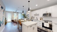 Located in Jacksonville, FL (32256), this single-floor 2-bedroom, 2-bathroom residence offers a thoughtfully designed layout with contemporary finishes throughout. The open-concept kitchen and living area serves as the heart of the home, anchored by a white quartz-topped island with bar seating and sleek black pendant lighting overhead. The kitchen is outfitted with crisp white shaker cabinetry, black hardware accents, a stainless steel undermount sink with a matte black faucet, white tile backsplash, and a full suite of stainless steel appliances. Light wood-style flooring runs throughout, enhancing the bright, airy atmosphere. The living room receives generous natural light through large windows dressed with sheer white curtains and wood blinds, creating a warm and inviting atmosphere. Both bedrooms are comfortably sized — the primary bedroom includes a ceiling fan, large windows with outdoor views, and dedicated closet space. The second bedroom mirrors a similarly cozy, well-lit design. Each of the two bathrooms features clean, modern finishes, with one showcasing a striking navy blue vanity with white countertops and a tub-shower combination. Two closets provide ample storage throughout the residence.