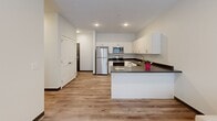 Located at 1810 K St in Lincoln, Nebraska, this thoughtfully designed 2-bedroom, 2-bathroom unit offers a clean, contemporary aesthetic throughout its single floor. The open-concept layout seamlessly connects the kitchen, dining, and living areas, creating an efficient and welcoming common space. The kitchen is well-appointed with white cabinetry, dark countertops, stainless steel appliances including a refrigerator, range, microwave, and dishwasher, all set above light hardwood-style flooring that flows consistently through the unit. The living area receives natural light through large windows and a glass door that opens onto a private patio, offering views of the surrounding neighborhood. Both bedrooms are comfortably sized, with the primary bedroom featuring a closet and easy access to one of the two full bathrooms. Each bathroom includes a tub-shower combination, white vanity with dark countertop, and a large mirror. Additional double-door closets provide ample storage, and a dedicated laundry area and utility room add practical convenience. The unit's neutral color palette, recessed lighting, and modern finishes contribute to a bright, clean ambiance throughout.