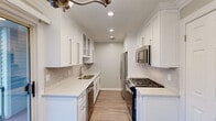 Located within Fairfield Townhouses at Holbrook on Saddle Rock Road in Holbrook, NY, this two-floor townhouse combines contemporary finishes with a functional, well-designed layout. Light wood-tone luxury vinyl plank flooring flows consistently throughout both levels, creating a clean and cohesive aesthetic.

The galley-style kitchen is a standout feature, outfitted with crisp white shaker cabinetry accented by brushed gold hardware, marble-look quartz countertops, and a matching tile backsplash. Stainless steel appliances, including a gas range, built-in microwave, refrigerator, and dishwasher, complete the space. Recessed lighting illuminates the kitchen efficiently.

The bedrooms are generously sized, each featuring crown molding, recessed lighting, and ceiling fans. Large windows invite natural light and offer views of surrounding greenery. At least one bedroom includes a walk-in closet with built-in shelving for added storage.

The bathroom showcases refined detailing, including a white vanity with marble-top counters, brushed gold fixtures, a medicine cabinet mirror with vanity lighting, wainscoting, and classic mosaic tile flooring.

A staircase with wood-tone treads and white risers connects the two floors, topped by a ceiling fan for added comfort. A dedicated laundry area with washer and dryer hookups is also present. Crown molding throughout adds an elegant finishing touch to this move-in-ready townhouse.