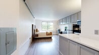 Located at 18 Old Ridgebury Rd in Danbury, CT, this thoughtfully designed studio-style unit offers a compact yet functional single-floor layout. The open-plan living and sleeping area is finished with light hardwood-style flooring and bright white walls, creating a clean and airy atmosphere. A large sliding window allows natural light to pour in while framing pleasant outdoor views of surrounding greenery, adding a sense of calm to the space.

The kitchen is well-appointed with gray shaker-style cabinetry extending to the ceiling for ample storage, stainless steel appliances including a refrigerator, electric range, and microwave, plus white countertops that keep the space feeling fresh and modern. A dedicated workspace with a desk is positioned near the window, making the unit versatile for both living and working. An in-unit washer adds everyday convenience.

The sleeping area accommodates a full-size bed with a stylish platform frame and integrated side tables, maximizing the use of the available footprint. The bathroom features light tile flooring, a granite-topped vanity, and a clean, functional layout. A closet rounds out the unit, providing essential storage. This space is ideal for those seeking a self-contained, efficiently designed residence in Danbury.
