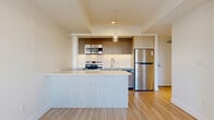 Located at 46 Flora St in Ottawa's centrally situated K2P neighbourhood, this well-appointed one-bedroom, one-bathroom unit offers a thoughtfully designed modern interior across a single floor. Light-toned laminate flooring runs throughout, complementing the clean white walls and creating a bright, cohesive aesthetic.

The open-concept kitchen, dining, and living area serves as the heart of the unit. The kitchen is outfitted with a full suite of stainless steel appliances — including a refrigerator, electric range, built-in microwave, and dishwasher — paired with two-tone cabinetry in light wood and charcoal finishes. A generous island with a light quartz-style countertop provides additional workspace and a natural division between the kitchen and living area. A pendant light fixture adds a stylish focal point overhead.

The bedroom is a well-proportioned, serene space featuring large sliding windows that frame views of the Ottawa cityscape and allow for ample natural light. A built-in sliding-door closet provides practical storage. The unit also includes two closets and an in-unit laundry area for added convenience.

The bathroom features light tile flooring, a glass-enclosed walk-in shower with wood-look tile surround, and clean, minimalist fixtures. The overall design of this unit emphasizes functionality and contemporary style in an efficient, well-organized layout.