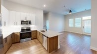 Located at 8120 Preston Road in Plano, TX, this thoughtfully designed 2-bedroom, 1-bathroom residence offers a clean, modern aesthetic across a single floor. The open-concept kitchen and living area serves as the heart of the home, anchored by a large center island with granite countertops, an undermount sink with a matte black faucet, and a white subway tile backsplash. The kitchen is outfitted with stainless steel appliances, including a French door refrigerator, electric range, built-in microwave, and dishwasher, complemented by a mix of white upper cabinetry and warm wood-toned lower cabinets. The adjoining living area benefits from a ceiling fan and natural light from multiple windows. Wood-look flooring flows seamlessly throughout the entire residence, adding warmth and continuity. The spacious primary bedroom features soaring ceilings, dual windows that invite natural light, and direct access to the full bathroom. The second bedroom includes a walk-in closet with built-in shelving. The bathroom is finished with a granite-topped wood vanity, matte black hardware, and a tub-shower combination. Neutral wall tones and clean lines give the entire space a fresh, contemporary feel.