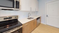 Located at 184 Pleasant St in Malden, MA, this single-floor unit presents a clean, modern aesthetic throughout. The main living area is bright and open, featuring light wood-tone flooring and neutral gray walls that create a fresh, airy atmosphere. Three windows along one wall allow natural light to fill the space while offering views of the surrounding neighborhood streetscape.

The layout flows naturally from the main living area toward the kitchen and additional rooms. The kitchen is outfitted with warm wood lower cabinetry paired with crisp white upper cabinets, a light quartz countertop, a stainless steel sink with a contemporary faucet, and stainless steel appliances including a range, dishwasher, and over-the-range microwave. The light flooring continues throughout, maintaining a cohesive look.

The bathroom features large-format neutral tile on both the floor and the tub surround, a wall-mounted floating vanity with open shelving, a wide frameless mirror, and a soaking tub with shower. White walls and streamlined fixtures complete the polished, contemporary feel. Overall, the unit offers a well-appointed, move-in-ready space with consistent modern finishes.