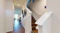 This two-story home opens into a welcoming entryway featuring warm hardwood-style flooring that extends throughout the main level. A natural wood console table and round black-framed mirror greet visitors upon entry, while recessed lighting illuminates the hallway leading toward the main living areas. A staircase with white-painted railings and wood-toned treads connects both floors, adding a classic architectural detail to the interior.

The main level includes an open living area anchored by a large sliding glass door that allows abundant natural light and provides direct access to an outdoor green space. A bold wall mural adds a striking artistic focal point to the room. The adjacent dining area features light-filled windows and connects seamlessly to the kitchen, which is equipped with white shaker cabinetry, granite countertops, a tile backsplash, and stainless steel appliances. A half bathroom with a small window completes the lower level.

Upstairs, the primary bedroom offers a calm, neutral aesthetic with hardwood-style flooring and recessed lighting. Throughout the home, a consistent palette of white walls and warm flooring creates a cohesive, modern feel.