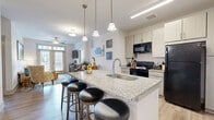 This two-bedroom, two-bathroom residence in Earlysville, Virginia offers a thoughtfully designed single-floor layout that balances comfort and functionality. The open-concept living, dining, and kitchen area forms the heart of the home, featuring light hardwood-style flooring throughout. The kitchen is equipped with granite countertops, light cabinetry, black appliances, and a central island with bar seating and pendant lighting. The dining area flows naturally from the kitchen and is illuminated by natural light. The living room includes French doors with transom windows that invite abundant natural light and outdoor views. Both bedrooms are carpeted and feature ceiling fans. The primary bedroom is generously sized, benefiting from multiple windows with outdoor views, and connects directly to a private en-suite bathroom. The second bedroom also offers comfortable proportions. Each bathroom is finished with granite-topped vanities and hardwood-style flooring; one includes a walk-in shower while the other features a full soaking tub. A spacious walk-in closet with wire shelving provides ample storage. The overall ambiance is clean and modern, with a neutral palette throughout.