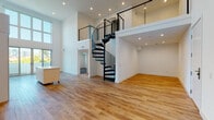 Located at 901 Vine St in the heart of Hollywood, Los Angeles, this modern two-story loft showcases a dramatic open-concept design defined by soaring double-height ceilings and an abundance of natural light. The main level features a spacious living area with warm hardwood flooring that flows seamlessly into a contemporary kitchen outfitted with sleek white cabinetry, stainless steel appliances including a gas range, microwave, and French door refrigerator, and a movable kitchen island. A wall of floor-to-ceiling windows floods the space with natural light while framing views of the surrounding neighborhood. A striking black spiral staircase serves as both a functional and architectural focal point, connecting the main level to the upper floor. The second level offers an open loft-style layout with cable-rail balcony overlooking the living area below, along with carpeted rooms that provide a quieter, more private retreat. Upper-level windows offer elevated views of the Los Angeles skyline, palm trees, and the rolling hills beyond. A clean, modern bathroom features marble-style tile surrounds a soaking tub and shower combination. Additional rooms on the upper level feature plush carpet, ample closet space, and recessed lighting, completing this sophisticated Hollywood loft.