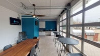 Located at 2650 Western Center Blvd in Fort Worth, Texas, this single-floor gathering space offers a dynamic and versatile environment suited for meetings, events, and social functions. The open-concept layout is defined by striking bold teal accent walls that contrast with crisp white finishes, creating an energetic yet polished atmosphere throughout.

The main area features a substantial live-edge wood communal table with ample seating, complemented by modern bistro-height tables and chairs that offer flexible arrangements. Large glass-paneled garage-style doors line one wall, flooding the interior with natural light and providing a seamless visual connection to the outdoor surroundings. When opened, these doors extend the usable space and create an airy, open-air feel.

A well-appointed kitchenette anchors one end of the space, outfitted with white cabinetry, dark countertops, an undermount sink, and upper storage — ideal for catering setups or light refreshment service. A wall-mounted flat-screen television is also present, supporting presentations and multimedia use.

The ceiling features a paneled design with a large ceiling fan that enhances air circulation, while tile flooring throughout provides durability and ease of maintenance. A secondary adjoining area with a glass entry door offers additional flexibility. Overall, this space combines functional amenities with a bold, modern aesthetic.