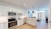 Located at Stadium Way in Madison, Alabama, this single-story unit offers a thoughtfully designed open-concept layout that seamlessly connects the kitchen, dining, and living areas. Light wood-style flooring runs throughout, providing a clean and cohesive aesthetic.

The kitchen is a standout feature, equipped with crisp white shaker cabinetry, a geometric patterned tile backsplash, quartz countertops, and a full suite of stainless steel appliances including a refrigerator, range, microwave, and dishwasher. A peninsula with pendant lighting above offers casual seating and additional prep space.

The living area is bright and welcoming, anchored by a ceiling fan and a set of full-length glass doors that invite natural light and provide outdoor access. The open sightlines between the kitchen and living space create an inviting, functional flow.

The bedroom is a calm retreat featuring a ceiling fan, a large window with blinds, and direct access to a generously sized walk-in closet outfitted with built-in shelving and hanging rods. The adjoining bathroom includes a tub-shower combination, a vanity with storage, and a two-tone color palette with gray accent walls complementing the white fixtures and trim throughout.