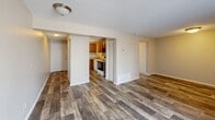 This single-floor unit at 2604 S Topeka St in Wichita, Kansas, offers a practical and efficiently organized layout. The open living area serves as the central feature of the space, finished with durable wood-look vinyl plank flooring in a warm gray-brown tone that extends throughout. A textured popcorn ceiling and neutral beige walls create a clean, understated backdrop. A large sliding glass door fitted with vertical blinds fills the living area with natural light and provides a view of the surrounding outdoor greenery.

The kitchen is positioned adjacent to the living space and is accessible via an open pass-through layout. It includes warm-toned wood cabinetry, a white electric range, a refrigerator, and a sink, offering essential functionality in a compact footprint. A dedicated closet provides additional storage within the unit.

The bathroom features a full-size soaking tub with a clean white surround that includes a built-in niche for storage, keeping the space tidy and functional. Flush-mount light fixtures provide consistent lighting throughout. The overall ambiance of the unit is straightforward and move-in ready, with consistent finishes that contribute to a cohesive, no-frills living environment.