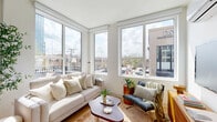 Located at 1529 N Fremont St in Chicago's vibrant Lincoln Park neighborhood, this thoughtfully designed two-bedroom, two-bathroom residence offers a modern living experience on a single floor. Light-filled and efficiently laid out, the space maximizes every square foot with clean lines and contemporary finishes throughout.

The open-concept kitchen and living area serves as the heart of the home. The kitchen features flat-front cabinetry in a warm taupe finish, stainless steel appliances, and a white quartz peninsula with bar seating — ideal for both cooking and casual dining. A large window floods the space with natural light and neighborhood views. The adjoining living room is anchored by expansive corner windows that frame dynamic city views, including a striking local street mural visible from the interior.

A private balcony extends the living space outdoors, offering open skyline and neighborhood views — a rare urban amenity. Light oak hardwood flooring runs seamlessly throughout, complementing the bright white walls and recessed lighting.

The primary bedroom is a serene retreat with a large window, wall-mounted HVAC, and ample natural light. The second bedroom mirrors this calm aesthetic. A bright hallway connects the rooms with understated mid-century accents. The bathrooms are finished with warm wood vanities and a standout tub surround featuring sage green checkerboard tile with a black-framed glass enclosure.