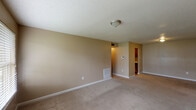 This single-floor, two-bedroom, one-bathroom unit is designed with a functional layout that makes efficient use of its space. The living area is generously sized, featuring neutral beige walls, plush carpeting, and a textured ceiling. Natural light enters through a large window and a rear door that provides direct outdoor access, lending the room an open, airy feel.

The galley-style kitchen runs parallel along two walls, lined with warm wood cabinetry and granite-look countertops. It is equipped with black appliances, including a refrigerator and electric range, alongside a double stainless steel sink. Wood-look flooring runs throughout the kitchen, offering a practical contrast to the carpeted areas.

Both bedrooms are comfortably proportioned with carpet flooring, textured ceilings, and windows fitted with blinds that allow for controlled natural light. The neutral color palette carries throughout, creating a cohesive and calm atmosphere across the unit.

The bathroom features a full tub-shower combination with clean white tile surround and chrome fixtures. Additional practical details include a recessed electrical panel, a wall-mounted thermostat, and a flush-mount ceiling light in the entryway hallway.