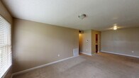 This single-floor, two-bedroom, one-bathroom unit is designed with a functional layout that makes efficient use of its space. The living area is generously sized, featuring neutral beige walls, plush carpeting, and a textured ceiling. Natural light enters through a large window and a rear door that provides direct outdoor access, lending the room an open, airy feel.

The galley-style kitchen runs parallel along two walls, lined with warm wood cabinetry and granite-look countertops. It is equipped with black appliances, including a refrigerator and electric range, alongside a double stainless steel sink. Wood-look flooring runs throughout the kitchen, offering a practical contrast to the carpeted areas.

Both bedrooms are comfortably proportioned with carpet flooring, textured ceilings, and windows fitted with blinds that allow for controlled natural light. The neutral color palette carries throughout, creating a cohesive and calm atmosphere across the unit.

The bathroom features a full tub-shower combination with clean white tile surround and chrome fixtures. Additional practical details include a recessed electrical panel, a wall-mounted thermostat, and a flush-mount ceiling light in the entryway hallway.