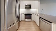 Located at 2475 Hurontario in Mississauga, Ontario, this well-appointed one-bedroom unit offers a thoughtfully designed layout across a single floor. Warm hardwood-style flooring flows seamlessly throughout, complementing the neutral, light-toned walls that create a bright and welcoming ambiance.

The open-concept living and kitchen area is the heart of the unit. The kitchen is outfitted with sleek white cabinetry extending to the ceiling, a marble-style tile backsplash, gray quartz countertops, and a full suite of stainless steel appliances including a French door refrigerator, slide-in range, built-in microwave, and dishwasher. A peninsula counter separates the kitchen from the living area, which features recessed pot lighting and an expansive, airy feel.

The bedroom is a comfortable and private retreat, featuring a mirrored sliding closet and a large floor-to-ceiling sliding glass door that opens directly onto a balcony. The balcony is also accessible from the living area, offering lush treetop views that bring a sense of nature into the unit. Natural light fills the space generously through oversized windows and the glass balcony door.

A bathroom with modern fixtures and an in-unit laundry area complete this well-equipped, move-in-ready space.