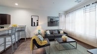 This well-appointed single-floor residence offers a thoughtfully designed layout that seamlessly connects the kitchen, dining, and living areas into a cohesive open-concept space. The kitchen is a standout feature, showcasing rich dark cabinetry, granite countertops, a double-basin stainless steel sink, and a full suite of stainless steel appliances including a range, over-the-range microwave, refrigerator, and dishwasher. A peninsula with bar seating provides a natural transition into the dining area, making the space ideal for both everyday living and entertaining.

The living room is bright and welcoming, benefiting from large windows dressed with sheer curtains and blinds that allow generous natural light to fill the room. Dark hardwood-style flooring runs consistently throughout the common areas and bedrooms, adding warmth and visual continuity to the space.

The residence includes multiple bedrooms, each offering a comfortable layout with ample natural light. The bathrooms are finished with granite-topped dark vanities and include a full tub and shower combination with clean, neutral tile work.

Overall, the space presents a modern and functional aesthetic, characterized by clean lines, neutral tones, and quality finishes that create an inviting and practical living environment.
