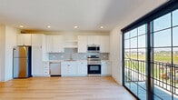 Located at 2295 SE Glacier Trl in Waukee, Iowa, this efficiently designed one-bedroom, one-bathroom unit offers a clean, modern aesthetic throughout its single floor. Light hardwood flooring flows consistently across every room, complementing the bright white walls and recessed lighting that keep the space feeling open and airy.

The combined kitchen and living area serves as the heart of the unit. The kitchen is outfitted with white shaker-style cabinetry, light countertops, a subtle tile backsplash, and a full suite of stainless steel appliances including a refrigerator, range, over-the-range microwave, and dishwasher. A large black-framed sliding glass door in the living area floods the space with natural light and provides direct access to a private balcony overlooking open outdoor scenery.

A hallway with a stylish sliding barn door connects the living area to the private quarters. The bedroom is a calm, well-proportioned retreat featuring a ceiling fan, recessed lighting, and a double sliding-door closet for convenient storage. An additional closet and a dedicated laundry area add practical functionality to the layout.

The bathroom maintains the unit's clean design with light flooring, white walls, black hardware accents, and a walk-in shower stall. The cohesive modern finishes throughout create a polished and comfortable living environment.