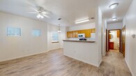 This two-floor residence offers a thoughtfully designed layout with clean, neutral finishes throughout. The main living area is open and airy, featuring light wood-look flooring, white walls, and a ceiling fan with integrated lighting. Natural light filters in through blinds-equipped windows, contributing to the bright and welcoming atmosphere.

The kitchen is positioned adjacent to the living space via a half-wall peninsula counter with a dark laminate surface, providing both a visual divider and casual seating opportunity. Warm honey-toned oak cabinetry lines the kitchen walls from counter to ceiling, offering generous storage. White appliances include a range, over-the-range microwave, and refrigerator. A built-in desk area adds functional workspace within the kitchen.

The bedrooms are carpeted and comfortably sized, each with a ceiling fan and windows for natural light. Closet space is provided via sliding-door or standard closets with built-in shelving. One bedroom connects directly to a bathroom featuring a single-sink vanity with oak cabinetry, granite-style countertop, a round mirror, and modern matte black fixtures. A secondary bathroom mirrors this aesthetic with an oval mirror and matching hardware. Light wood-look flooring is consistent across the non-carpeted areas, tying the overall design together cohesively.