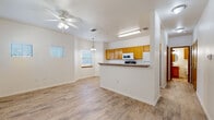 This two-floor residence offers a thoughtfully designed layout with clean, neutral finishes throughout. The main living area is open and airy, featuring light wood-look flooring, white walls, and a ceiling fan with integrated lighting. Natural light filters in through blinds-equipped windows, contributing to the bright and welcoming atmosphere.

The kitchen is positioned adjacent to the living space via a half-wall peninsula counter with a dark laminate surface, providing both a visual divider and casual seating opportunity. Warm honey-toned oak cabinetry lines the kitchen walls from counter to ceiling, offering generous storage. White appliances include a range, over-the-range microwave, and refrigerator. A built-in desk area adds functional workspace within the kitchen.

The bedrooms are carpeted and comfortably sized, each with a ceiling fan and windows for natural light. Closet space is provided via sliding-door or standard closets with built-in shelving. One bedroom connects directly to a bathroom featuring a single-sink vanity with oak cabinetry, granite-style countertop, a round mirror, and modern matte black fixtures. A secondary bathroom mirrors this aesthetic with an oval mirror and matching hardware. Light wood-look flooring is consistent across the non-carpeted areas, tying the overall design together cohesively.