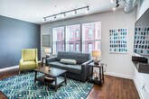 This single-floor, 1-bedroom, 1-bathroom residence in Memphis, TN offers a thoughtfully designed layout that maximizes both comfort and functionality. The open-concept living area is highlighted by warm hardwood flooring, track lighting with an industrial-chic edge, and large windows dressed with blinds that invite generous natural light and views of the surrounding streetscape. The living room comfortably accommodates a seating arrangement centered around a coffee table, with accent seating and a wall-mounted television, creating an inviting space for relaxation.

The kitchen is a standout feature, boasting rich wood cabinetry, granite countertops, a peninsula with bar seating, and a full suite of stainless steel appliances including a refrigerator, range, and microwave. Track lighting overhead enhances both visibility and ambiance in this functional yet stylish cooking space.

The bedroom is a serene retreat, featuring a ceiling fan, crisp white walls, hardwood floors, and a walk-in closet providing ample storage. The bathroom continues the warm aesthetic with hardwood-style flooring, a rich wood vanity, granite countertop, a large mirror, and a shower-tub combination. Throughout the unit, a cohesive color palette and modern finishes create a polished, comfortable living environment.