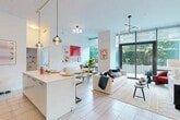 Located in Miami's dynamic Edgewater neighborhood, this bright and contemporary 2-bedroom, 2-bathroom residence offers a thoughtfully designed single-level layout filled with natural light. The open-concept living, dining, and kitchen area forms the heart of the home, anchored by large floor-to-ceiling glass windows and sliding doors that connect seamlessly to a generous wraparound balcony. The outdoor space is framed by manicured tropical landscaping, including palm trees and lush hedging, creating a private urban retreat. The modern kitchen is outfitted with sleek dark cabinetry, stainless steel appliances, a tiled backsplash, and a white waterfall island with bar seating, all accented by stylish pendant lighting. Light-toned tile flooring flows throughout the entire residence, enhancing its clean, airy aesthetic. The primary bedroom is a well-proportioned suite featuring floor-to-ceiling windows with outdoor views and direct balcony access. The second bedroom also benefits from generous glazing and soaring ceilings with an architectural arched window detail. Both bathrooms are finished in a crisp, minimalist style with white cabinetry and framed mirrors. Additional highlights include a dedicated laundry closet with a stacked washer and dryer, multiple storage closets, and a welcoming entrance hallway.