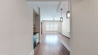 This well-designed single-story residence offers 1090 square feet of comfortable living space, including two bedrooms and two bathrooms. The home's layout is thoughtfully planned, with a focus on maximizing space and functionality. The primary bedroom, at 190 square feet, provides a generous retreat for homeowners.

The heart of the home is an open-concept living area, which likely combines the kitchen and living room for a spacious, contemporary feel. The image showcases a portion of this area, revealing beautiful wood flooring that adds warmth and character throughout. Recessed lighting in the ceiling ensures even illumination, while a glass-paneled door with a transom window above invites natural light to flood the space.

The home's neutral color palette, with light walls and trim, creates a bright and airy atmosphere. This versatile backdrop allows for easy personalization to suit various tastes and styles. Two hallways and two closets provide additional storage and ease of movement throughout the home.

While specific details about the kitchen and bathrooms are not provided, the overall quality and attention to detail evident in the visible areas suggest these spaces are likely well-appointed and functional. The combination of modern amenities and thoughtful design makes this property an attractive option for those seeking a comfortable, efficient living space.