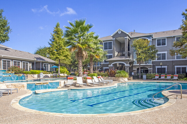 Austin, TX Apartments - Vista de la fachada del edificio Nolina Flats Apartments rodeada de frondosos paisajes con vistas de la piscina - Nolina Flats