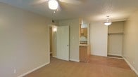 This single-floor residential space offers a practical and comfortable layout designed for everyday living. The main living area is carpeted and benefits from ceiling-mounted lighting, creating a warm and inviting atmosphere. Neutral-toned walls throughout lend the space a clean, versatile aesthetic.

Adjacent to the living area, the kitchen is equipped with wooden cabinetry offering ample storage, a sink, and a breakfast bar that serves as both a functional workspace and a casual dining surface. The kitchen connects seamlessly to the living space, supporting an open feel that encourages interaction between areas.

A doorway from the main living area leads into an interior hallway, providing access to additional rooms within the unit. The hallway is well-lit, contributing to an overall sense of openness. Overhead ventilation is visible throughout, ensuring proper airflow.

The textured ceiling adds a subtle architectural detail, while consistent flooring and wall finishes tie the spaces together cohesively. Overall, the layout is straightforward and functional, making efficient use of the available space while maintaining a comfortable residential ambiance suited to a variety of living arrangements.