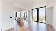 Located on Peachtree Street in Atlanta's vibrant Midtown neighborhood, this contemporary residence offers five bedrooms and three bathrooms across a single thoughtfully designed floor. The open-concept kitchen and living area serves as the heart of the home, showcasing floor-to-ceiling windows that frame breathtaking panoramic views of the Atlanta skyline and lush treetop canopy below. The kitchen features a large island with a stone countertop, warm wood lower cabinetry, crisp white upper cabinets, a subway tile backsplash, and stainless steel appliances. Rich hardwood flooring flows throughout the living areas and bedrooms, enhancing the bright, airy atmosphere. The primary bedroom benefits from expansive glazing with sweeping city views and connects to a spacious walk-in closet with built-in shelving and hanging systems. The primary bathroom is elegantly appointed with a dual-sink vanity in wood and stone finishes, a glass-enclosed shower, a soaking tub, and large-format tile flooring. Additional bathrooms include tiled tub-shower combinations. A hallway with in-unit stacked laundry adds everyday convenience. Clean white walls, modern panel doors with matte black hardware, and recessed lighting complete the sophisticated, contemporary aesthetic throughout.