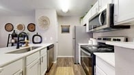 Located at 5909 Valleycreek Ln in Arlington, TX, this well-appointed one-bedroom, one-bathroom home offers a thoughtfully designed single-floor layout that maximizes every inch of its cozy footprint. The galley-style kitchen is outfitted with white shaker cabinetry, white countertops, and a full suite of stainless steel appliances, including a refrigerator, electric range, microwave, and dishwasher. Wood-look flooring runs throughout the kitchen and living areas, adding warmth and continuity. A breakfast bar with seating opens the kitchen toward the living room, creating an inviting, connected feel. The living room is bright and airy, anchored by a ceiling fan and a sliding glass door that ushers in natural light and leads to an outdoor patio. A textured ceiling adds dimension overhead. The bedroom features plush carpet, a natural window that brings in soft light, and a walk-in closet offering generous storage. The bathroom is clean and functional, with a white vanity, ample counter space, a tub-shower combination, and wood-look flooring that ties in with the rest of the home. A connecting hallway links all rooms efficiently, completing this compact yet comfortable layout ideal for everyday living.