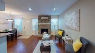 This two-floor residence in Houston's 77063 neighborhood offers a well-organized layout with distinct living, dining, kitchen, and sleeping spaces spread across both levels. The main living area makes an immediate impression with its rich hardwood flooring, a classic brick fireplace flanked by windows dressed in sheer curtains, and recessed lighting that creates a warm, inviting ambiance.

The kitchen is positioned as a central hub, featuring a peninsula with granite countertops, white cabinetry, black appliances including a full-size refrigerator and range, and tile flooring that transitions seamlessly from the hardwood in the adjacent areas. A dedicated dining space sits nearby, illuminated by a pendant light fixture and accented by wall-mounted shelves and a window that brings in natural light.

The living room offers a comfortable layout with a ceiling fan, natural light through a window with sheer curtains, and hardwood floors throughout. Bedrooms are carpeted for comfort; the primary bedroom is generously proportioned with a ceiling fan and en-suite access, while the secondary bedroom functions well as a dual-purpose sleeping and workspace. Both bathrooms feature granite-topped white vanities with large mirrors and tile flooring.