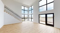 Located at 1115 Locust Ave in Long Beach, CA, this contemporary two-story space showcases a striking modern design defined by clean lines, a crisp white palette, and light natural hardwood flooring throughout. The main living area commands immediate attention with its dramatic double-height ceilings and an expansive wall of floor-to-ceiling black-framed windows that flood the interior with natural light and frame sweeping views of the Long Beach skyline. A sleek staircase with a minimalist metal railing leads to the upper level, enhancing the open, airy atmosphere. A private balcony, accessible via large glass doors, extends the living space outdoors and further capitalizes on the elevated city views. The kitchen is well-appointed with flat-front white cabinetry extending to the ceiling, a textured grey tile backsplash, stainless steel appliances including a gas range, built-in microwave, dishwasher, and a French door refrigerator. The bedrooms are generously sized, finished with the same warm hardwood flooring, and feature large black-framed windows offering additional city and neighborhood views. The bathroom presents a refined aesthetic with white subway tile, a soaking tub with glass enclosure, matte black fixtures, and a speckled terrazzo floor.
