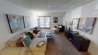 This single-floor residence offers a thoughtfully organized layout across several distinct living areas. The living room serves as the central gathering space, featuring wall-to-wall carpet, a textured ceiling, and large sliding glass doors that open to a balcony, allowing natural light to fill the room. A dedicated media wall accommodates an entertainment unit, while generous floor space supports flexible furniture arrangements.

The kitchen is well-equipped with rich dark-stained cabinetry, granite-style countertops, and a full suite of black appliances including a range, dishwasher, microwave, and refrigerator. Track lighting overhead illuminates the wood-look flooring, contributing to a warm, functional workspace.

Adjacent to the kitchen, the dining area provides a comfortable setting for everyday meals, featuring wood-look flooring consistent with the kitchen and a simple overhead fixture.

The primary bedroom is generously sized with a large picture window providing ample natural light, while the secondary bedroom includes an open closet and neutral finishes. The bathroom features a wide vanity with a large mirror, dark cabinetry, and wood-look flooring, with a shower-tub combination completing the space.